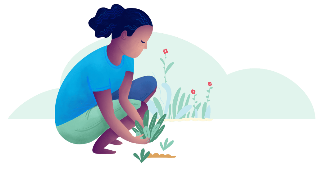 A person crouches beside a patch of soil, lowering a small plant into the ground